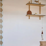 Verticale behangrand Wieber van Bibelotte in oker langs een witte wand met houten wandplanken