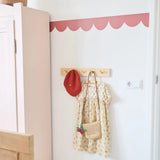 Witte kinderkamerwand met een roze golvende behangrand van Bibelotte boven een houten kapstok