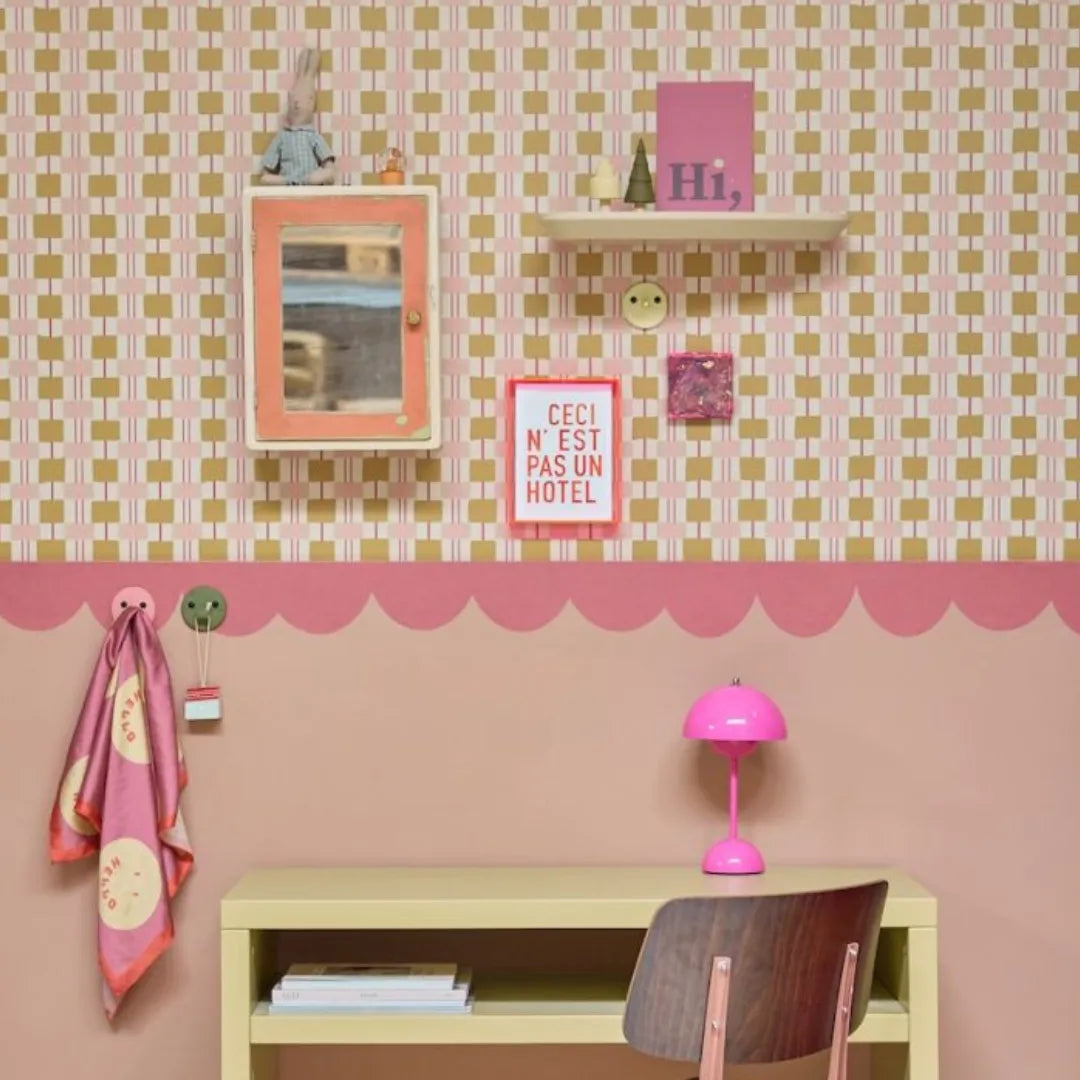 Kinderkamer met okergeel blokjesbehang en een roze golvende behangrand van Bibelotte boven een roze muur