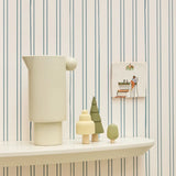 Gestreept petrol behang van Bibelotte achter een wandtafel met houten boompjes